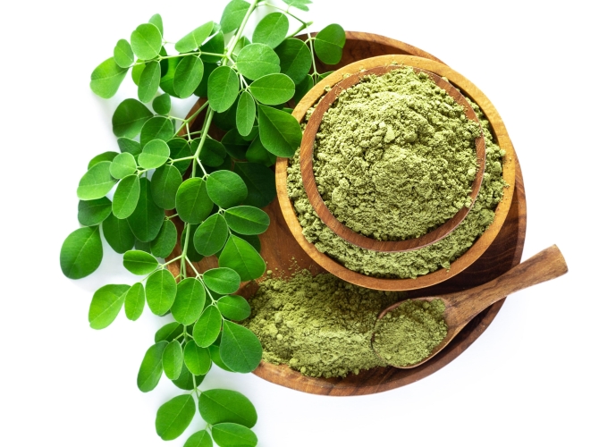 Moringa powder (Moringa Oleifera) in wooden bowl with original fresh Moringa leaves isolated on white background. Healthy product, superfood, vitamin. Top view.